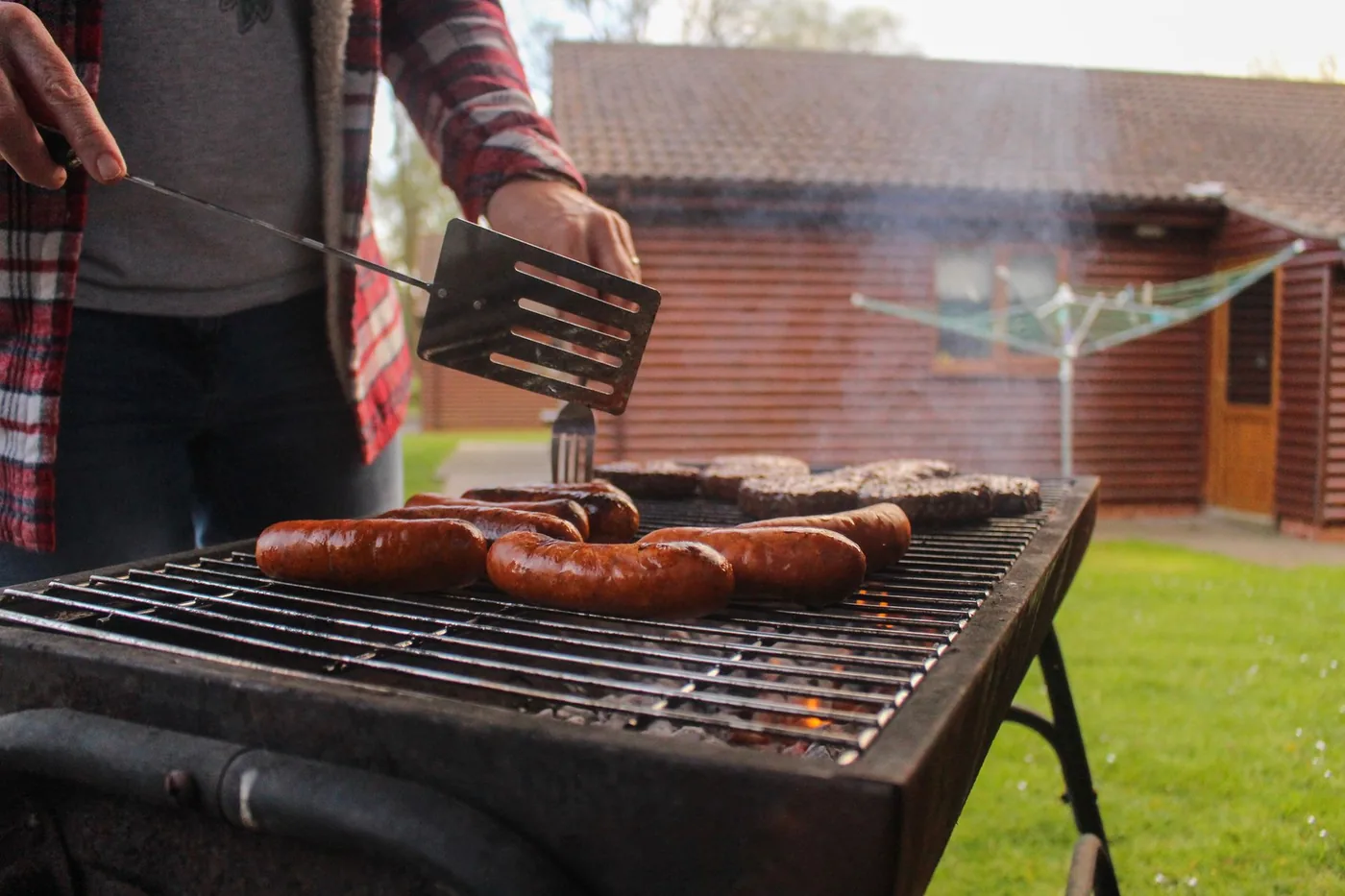 Muž griluje párky na zahradním grilu