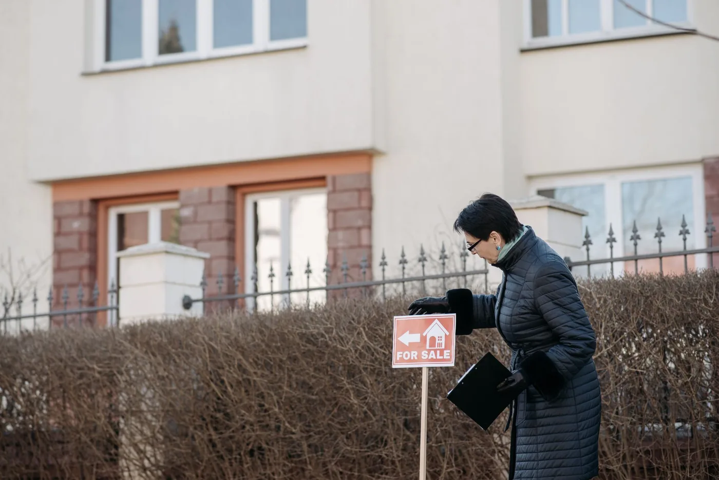 Žena upevňuje prodejní ceduli před domem