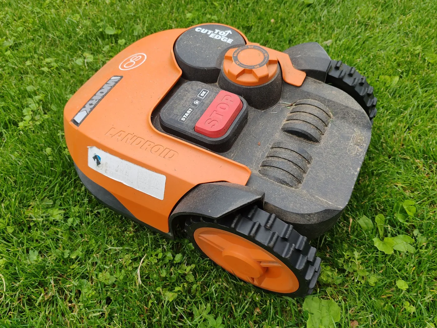 Detail oranžové robotické sekačky na trávníku