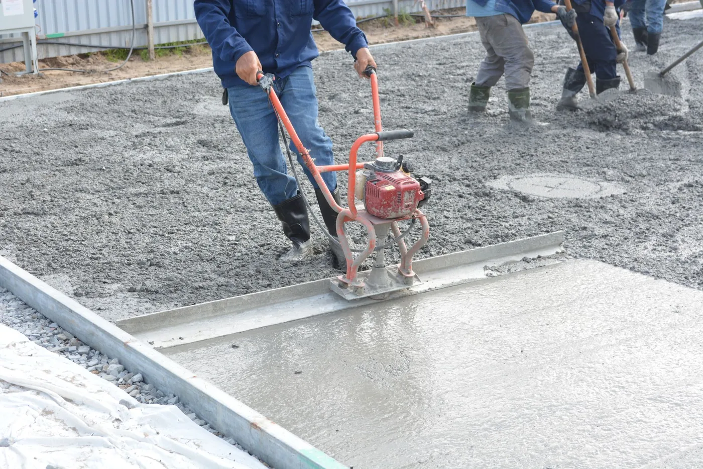 Dělník uhlazuje čerstvě litý beton vibrační latí